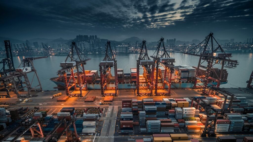 Container ship loaded by cranes at a busy port at dusk